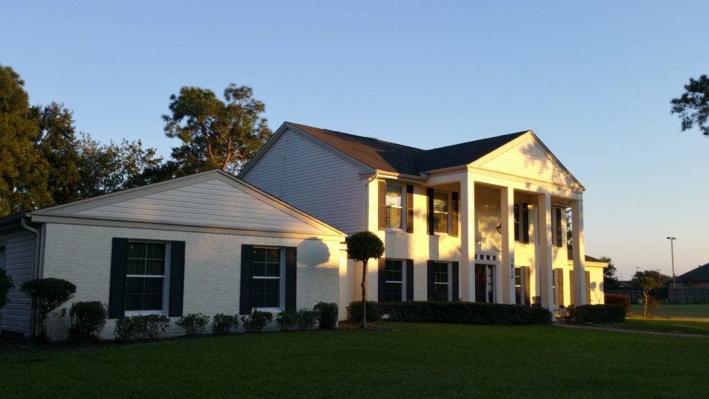 Two-story white house with columns and a dark shingle roof at sunset