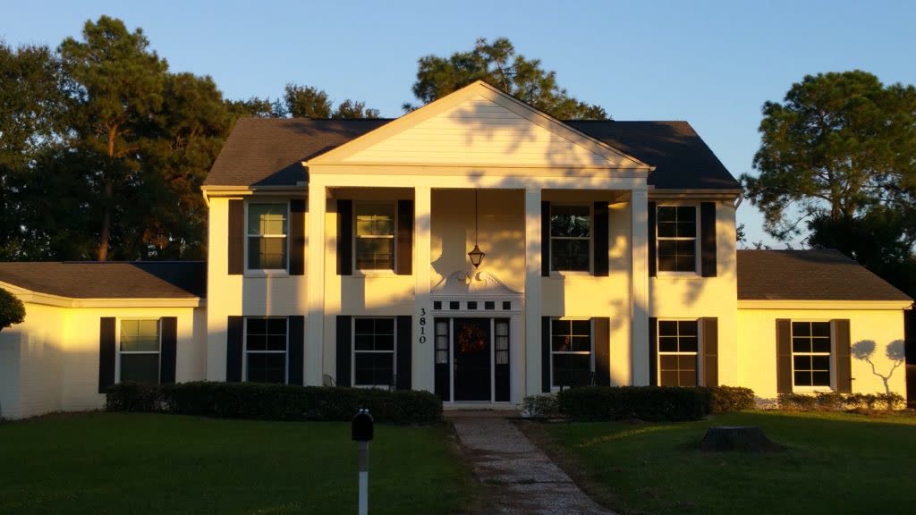 White two-story colonial house with dark shingle roof in evening light